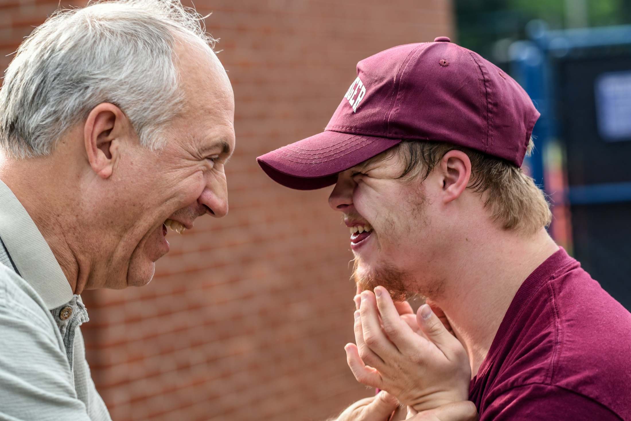 An older man and a young man share a laugh outdoors.