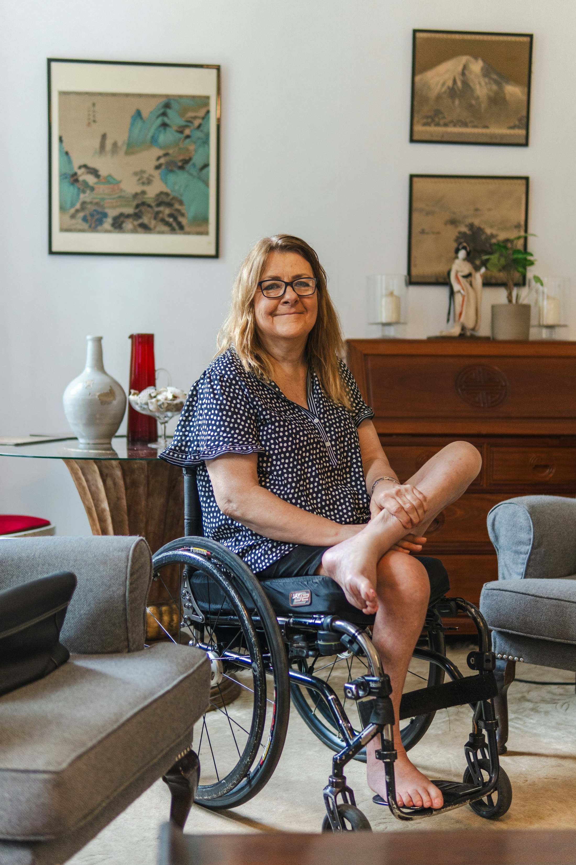 A woman in a wheelchair smiles in her living room.