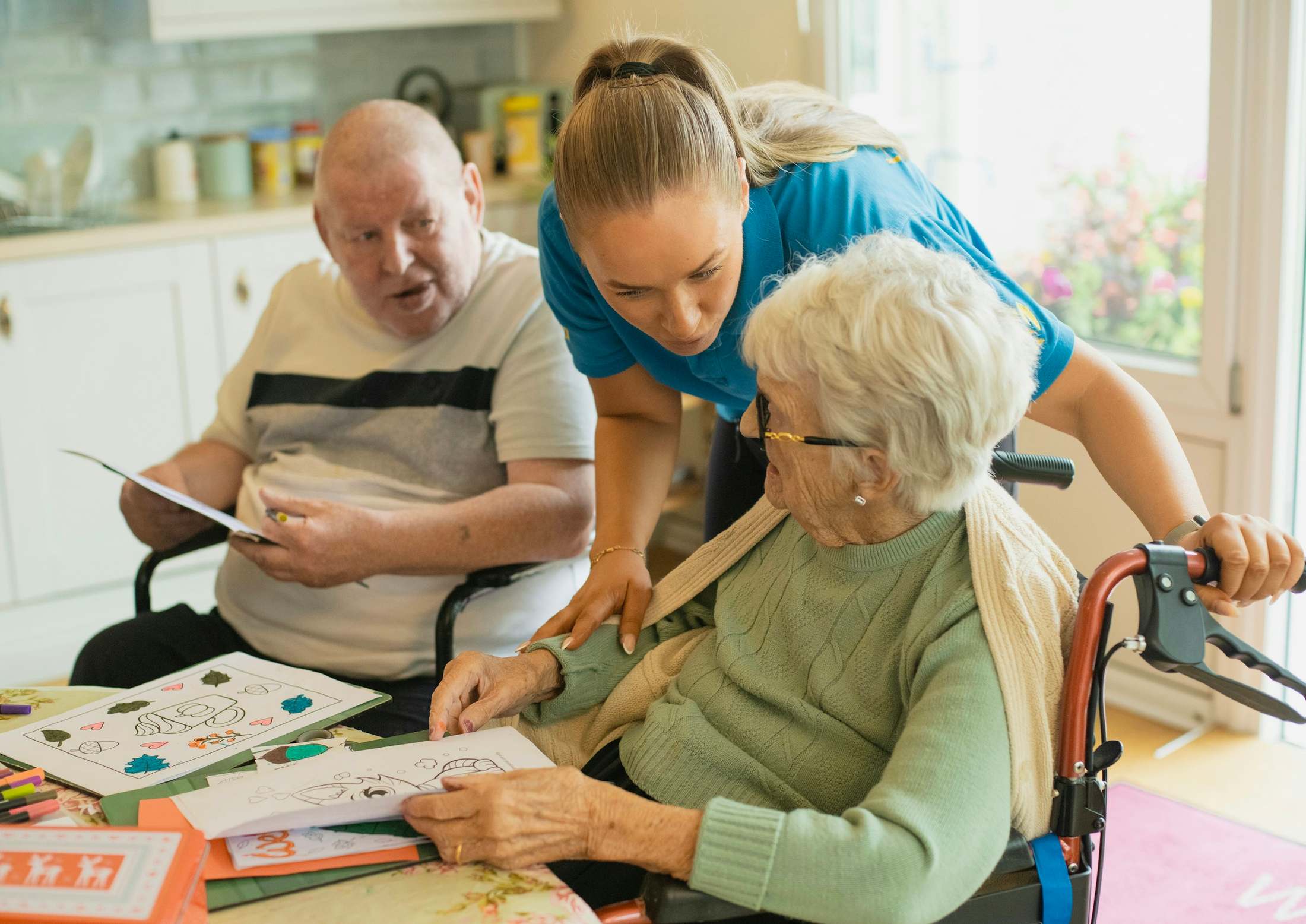 A caregiver leans in to help an older couple at a table.