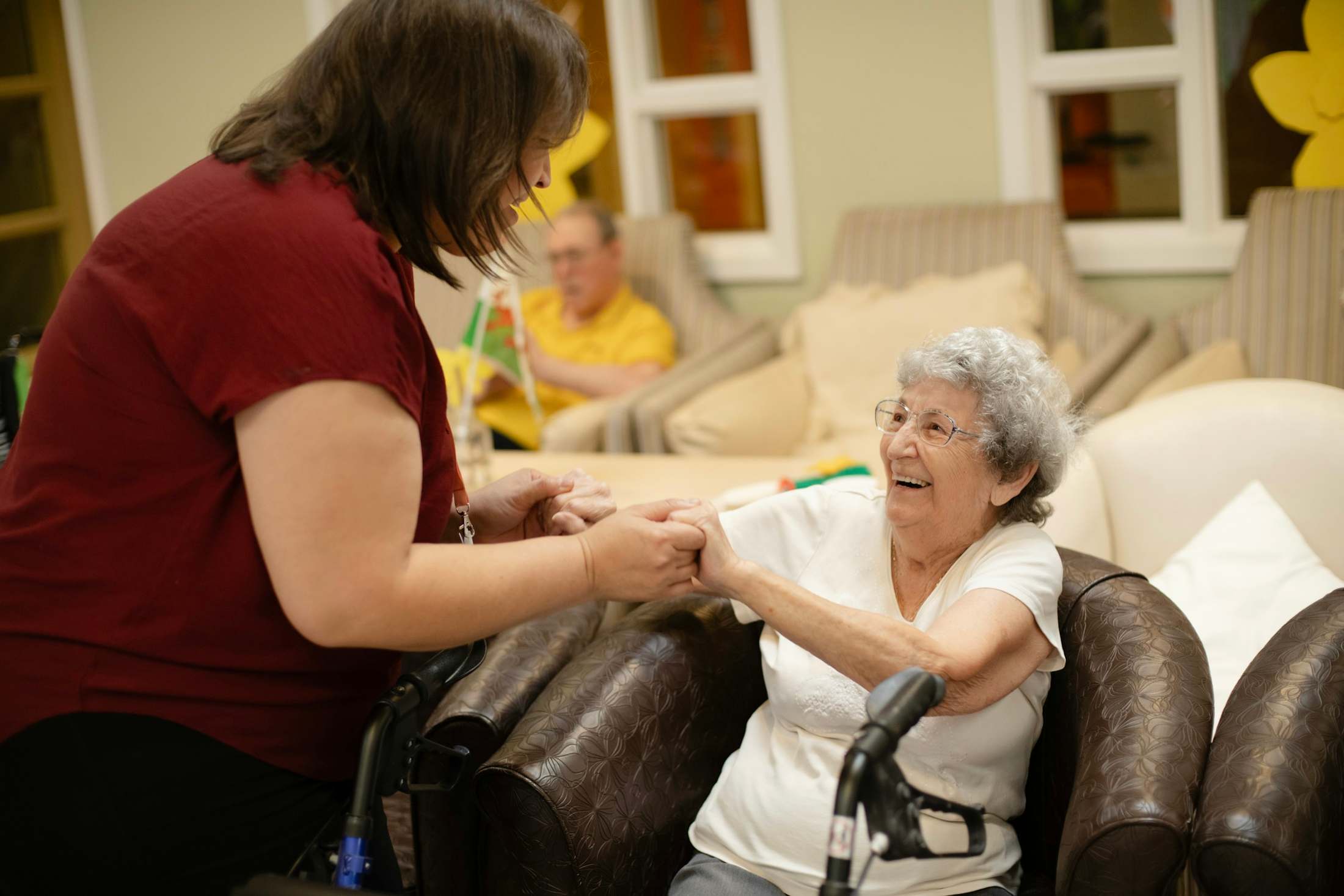 A caregiver and an older woman laugh together in a living room.