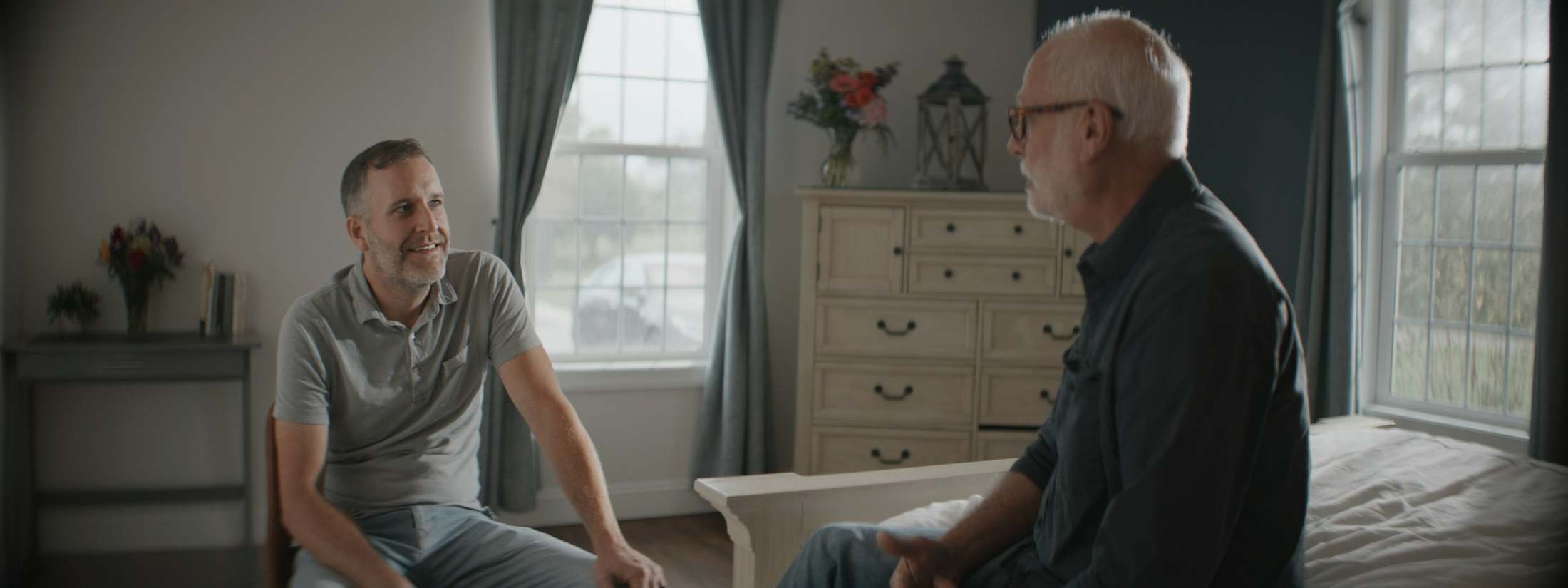 Two men talk in a warmly lit room.